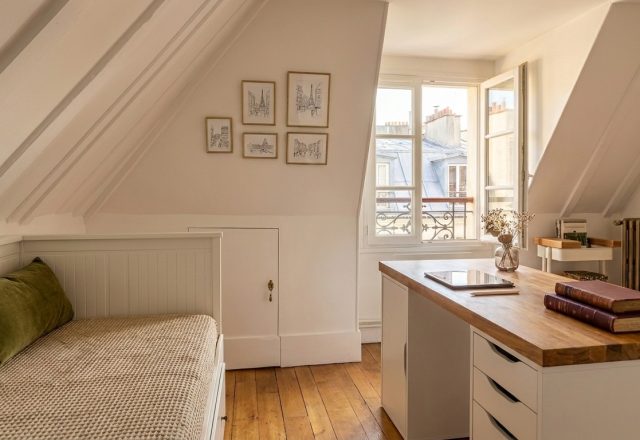 A bright attic home office layout featuring a wooden desk, white drawers, and a built-in daybed under slanted ceilings.