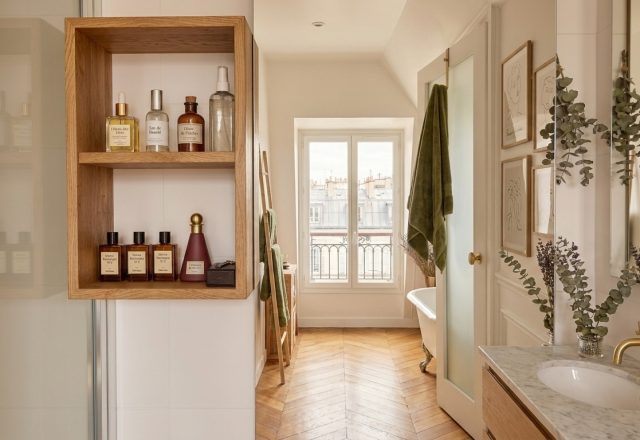 Modern primary bathroom featuring built-in wooden shelving, marble vanity, and chevron flooring.