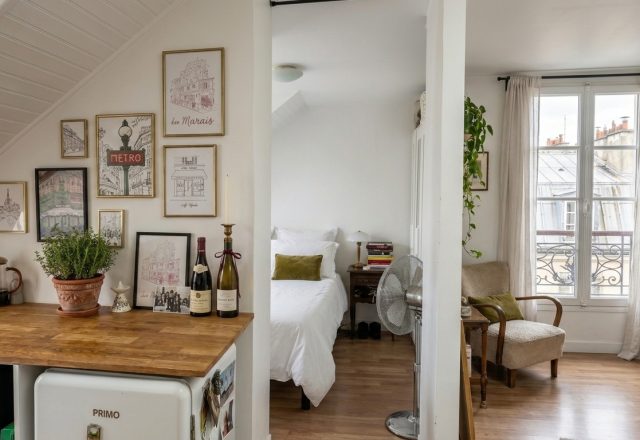 Bright small studio layout featuring an open kitchen, partitioned bedroom alcove, and sunlit sitting area.