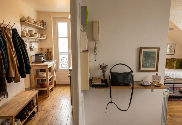 Small entryway organization featuring a wooden coat rack, shoe bench, and a floating shelf in a narrow hallway