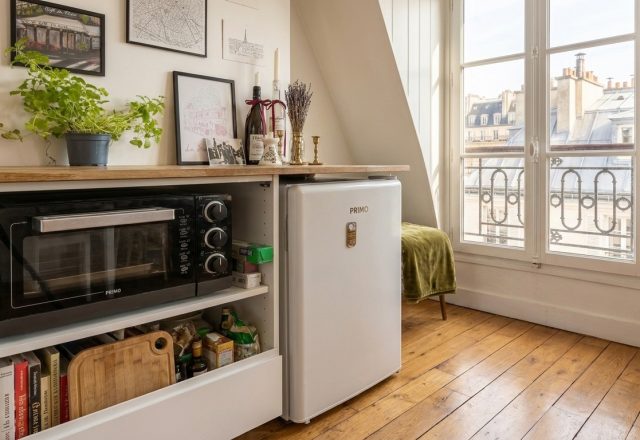A smart small kitchen layout featuring a compact oven, mini fridge, and wooden countertop beneath an attic window.