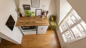 A clever small kitchen layout featuring a wooden countertop over a compact fridge, microwave, and bright window.