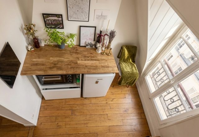 A clever small kitchen layout featuring a wooden countertop over a compact fridge, microwave, and bright window.