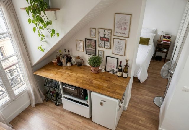 A smart small studio kitchen layout featuring a wooden counter under-stair, mini fridge, and rolling storage carts.