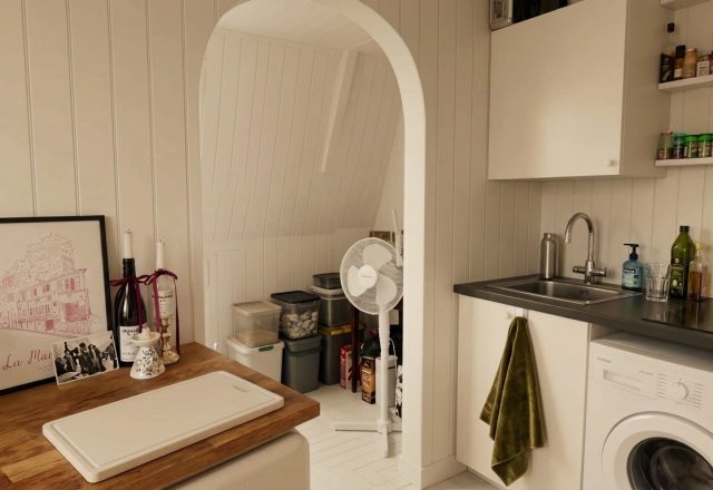 Bright small utility room design featuring white panel walls, compact laundry appliances, and open shelving.
