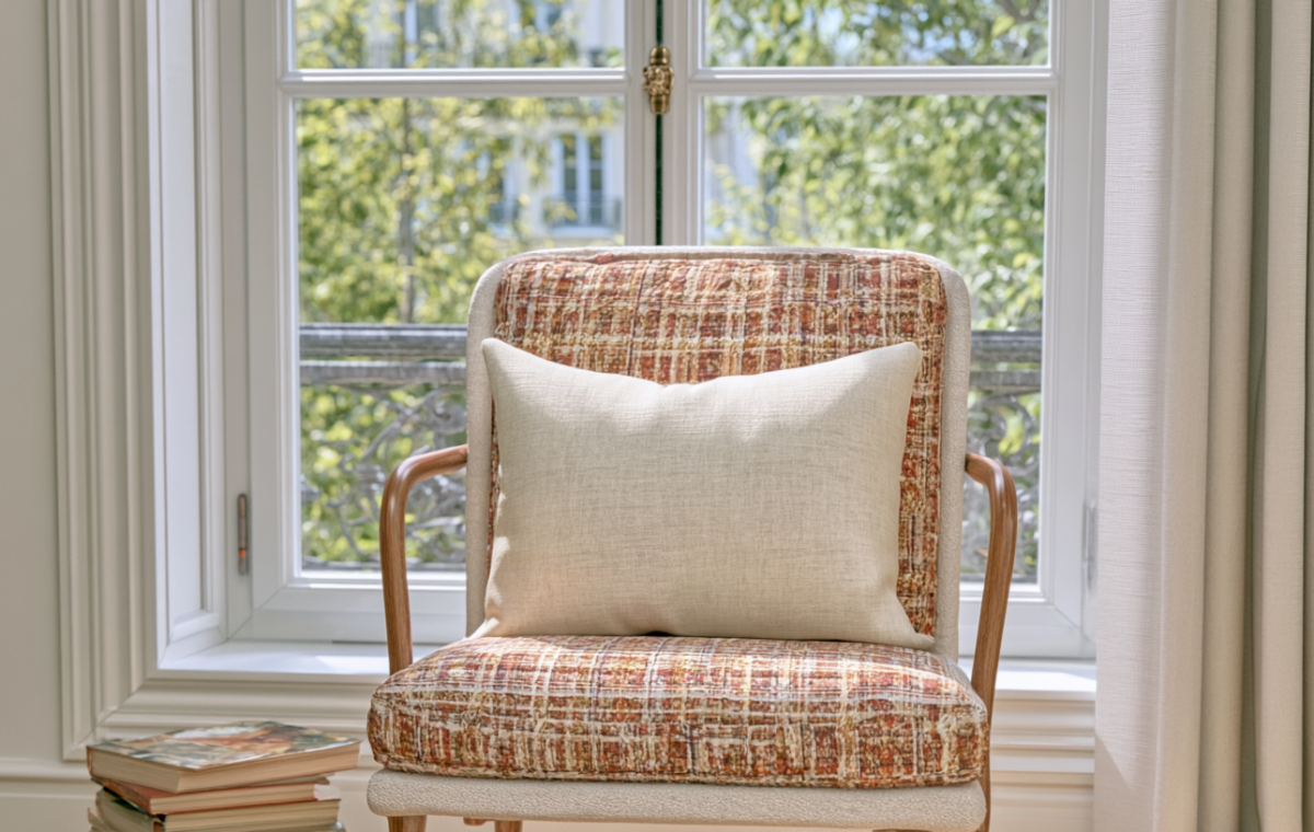 Cozy reading nook featuring a textured plaid armchair with a neutral linen cushion and stacked books near a sunny window.