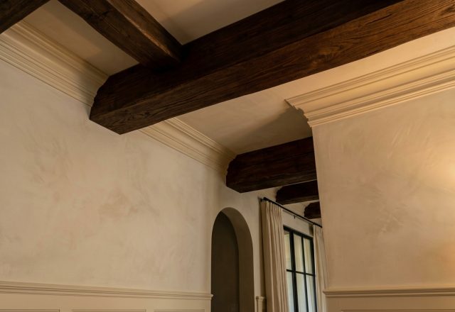 Dark wood ceiling beams contrasted against textured plaster walls in a transitional style living room.