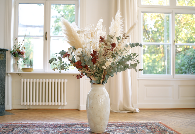A large dried floral arrangement featuring pampas grass and eucalyptus inside a ceramic vase in a living room.