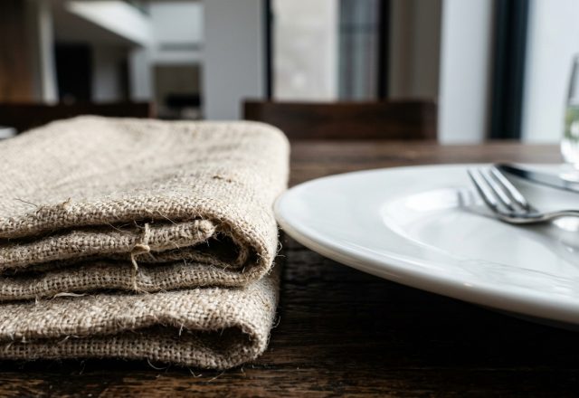 Close up of a rustic table setting with linen napkins and white plates on wood.