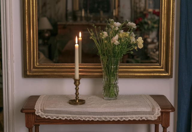 An antique console table styled with a brass candlestick and fresh flowers beneath a vintage mirror.