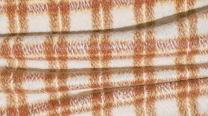 Close-up shot of a cozy rust orange and cream wool plaid throw blanket with soft brushed texture.