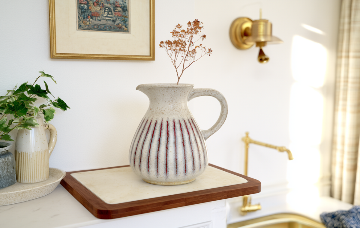 A speckled ceramic jug vase with red stripes styled on a wooden board with dried botanicals in a bright kitchen.