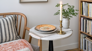 A cozy living room corner featuring a stone accent table, lit candle, and striped cushion chair in English style.