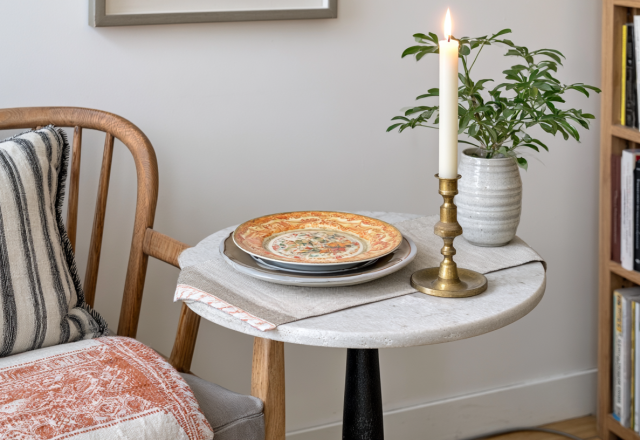 A cozy living room corner featuring a stone accent table, lit candle, and striped cushion chair in English style.