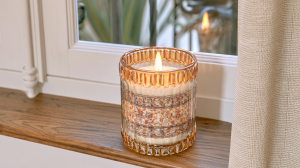 Decorative glass candle jar with a floral pattern sitting on a wooden windowsill.