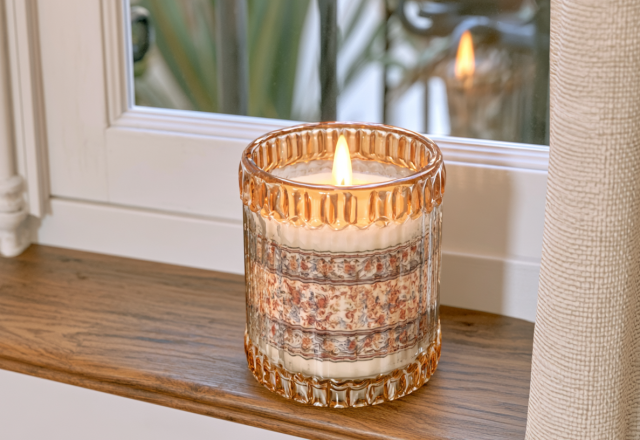 Decorative glass candle jar with a floral pattern sitting on a wooden windowsill.