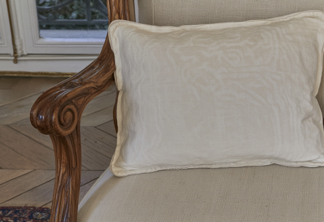 A simple neutral accent pillow placed on a classic wooden armchair in a sunlit room.