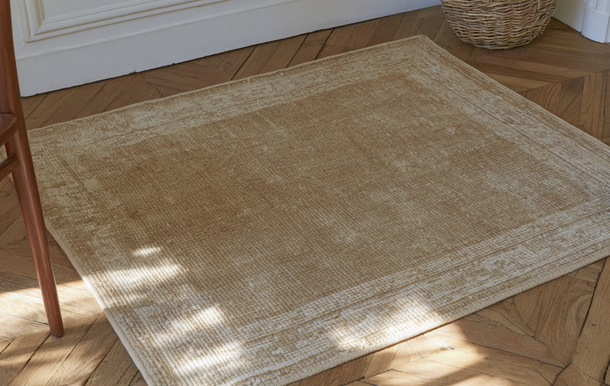 A neutral area rug placed on herringbone wood floors next to a wooden chair.