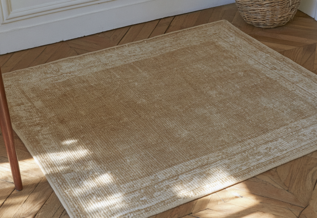 A neutral area rug placed on herringbone wood floors next to a wooden chair.