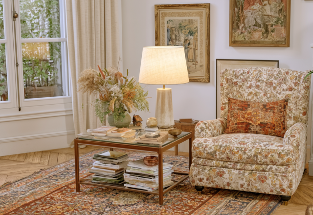 A cozy living room featuring a patterned armchair, glass coffee table, and traditional art.