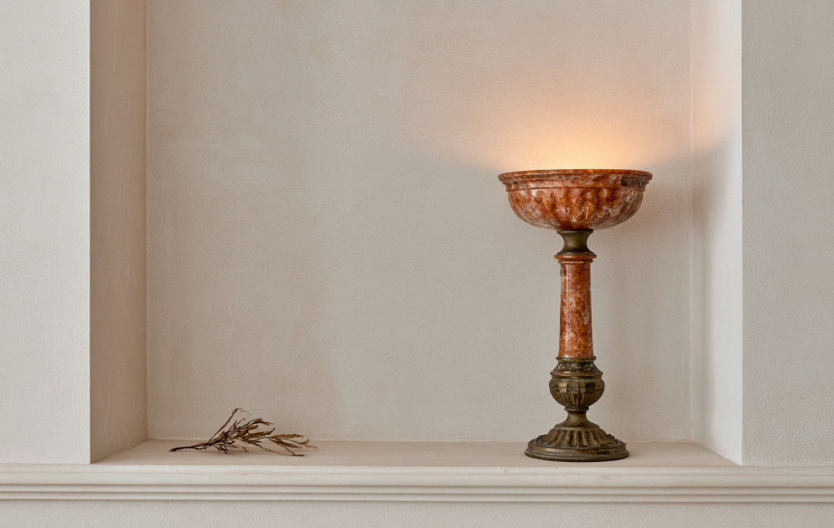 A vintage stone urn lamp with warm amber lighting resting inside a neutral recessed wall alcove.
