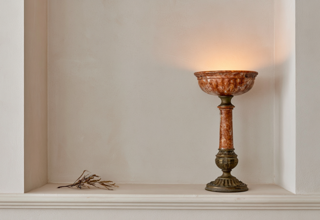 A vintage stone urn lamp with warm amber lighting resting inside a neutral recessed wall alcove.