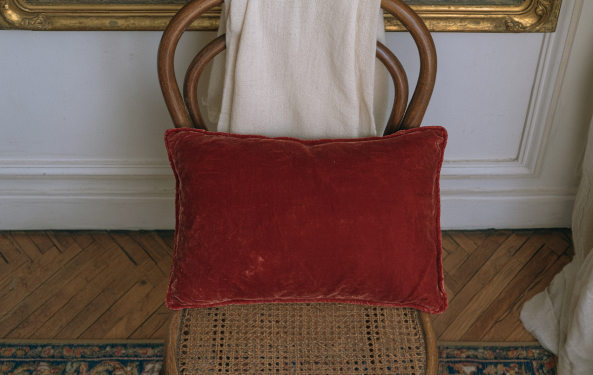 A plush red velvet accent pillow resting on a vintage cane chair against a neutral wall.
