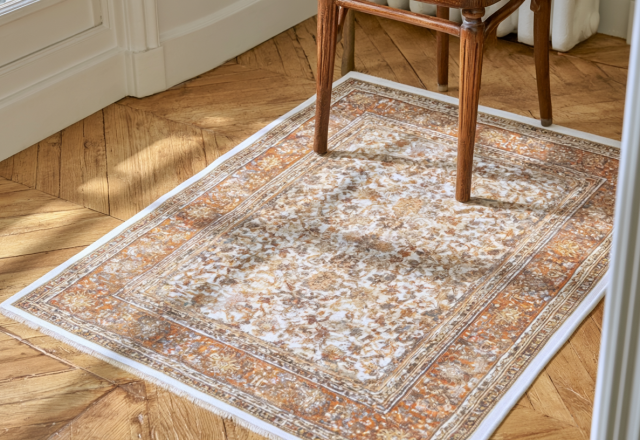 A distressed vintage area rug with rust and cream patterns resting on classic herringbone wood floors.