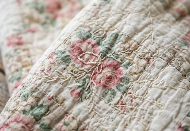 Close-up of a vintage floral quilt with hand-stitched details resting on a rustic surface.