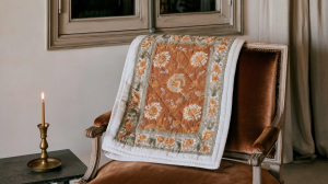 A vintage floral quilt draped over a brown velvet armchair next to a brass candlestick.