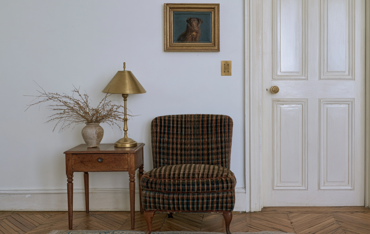 Vintage plaid armchair next to a wooden side table with a brass lamp and framed dog painting.