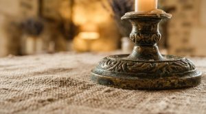 Close up of an ornate antique brass candle holder sitting on a textured linen table runner.