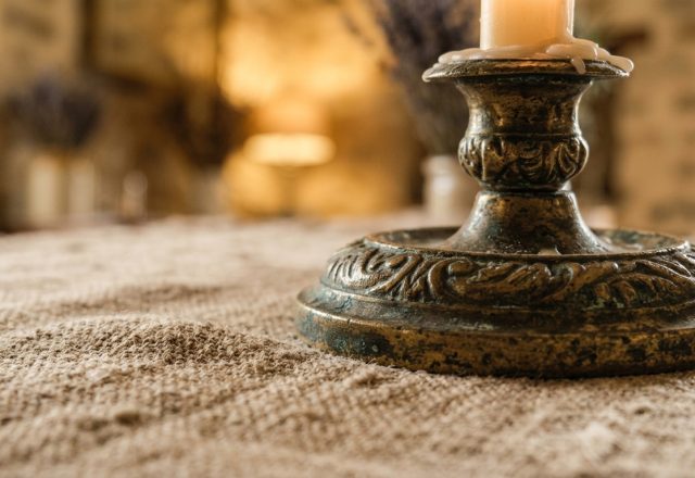 Close up of an ornate antique brass candle holder sitting on a textured linen table runner.