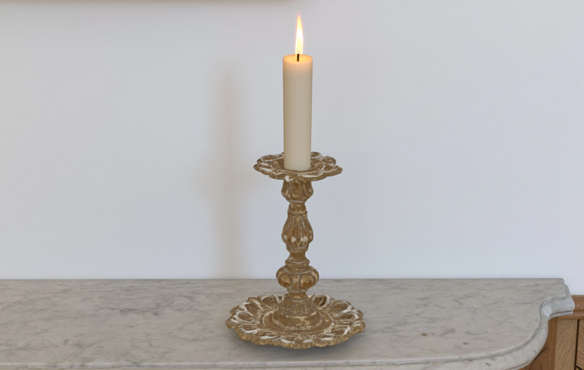 An antique brass candlestick holder with a lit white taper candle sitting on a marble console table.