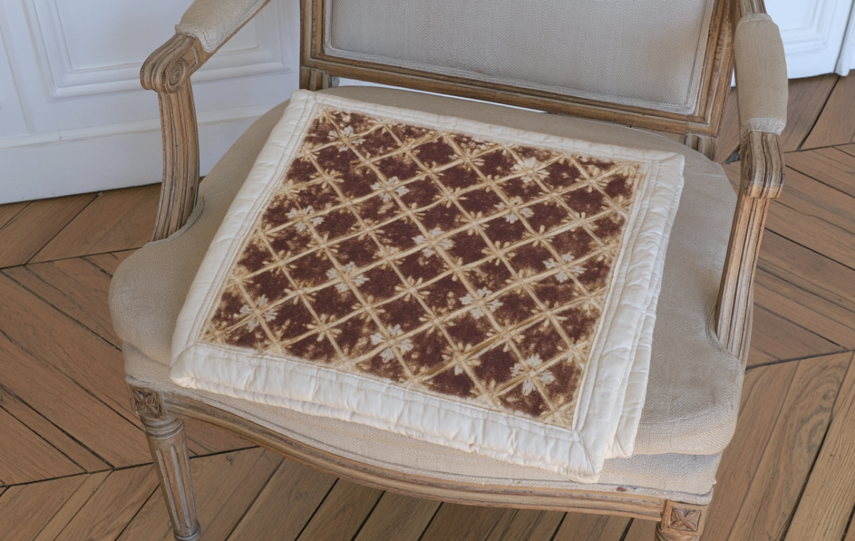 A patterned quilted antique chair cushion resting on a vintage wooden armchair.