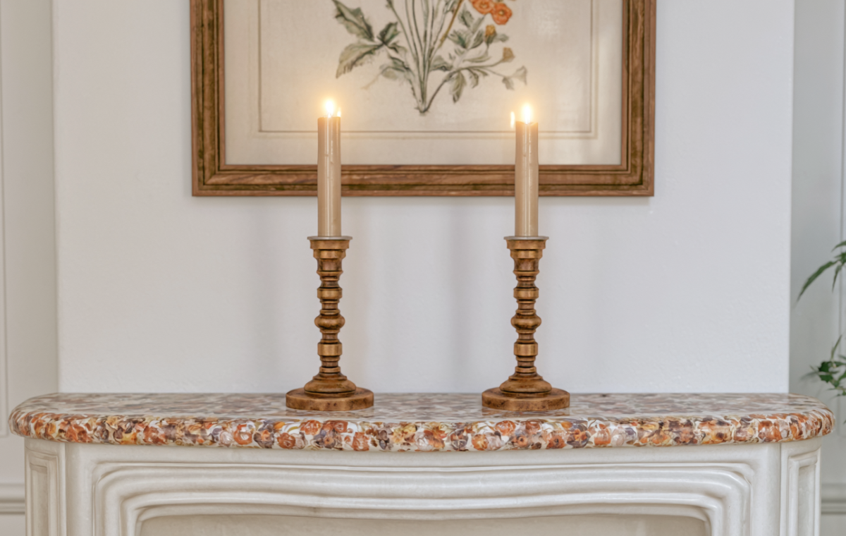 Two brass mantel candle holders with lit candles placed on a decorative marble fireplace shelf.