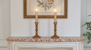 Two brass mantel candle holders with lit candles placed on a decorative marble fireplace shelf.