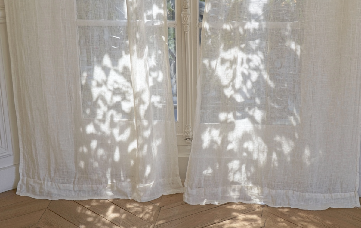 Sunlight filtering through sheer linen curtains onto wooden parquet flooring.