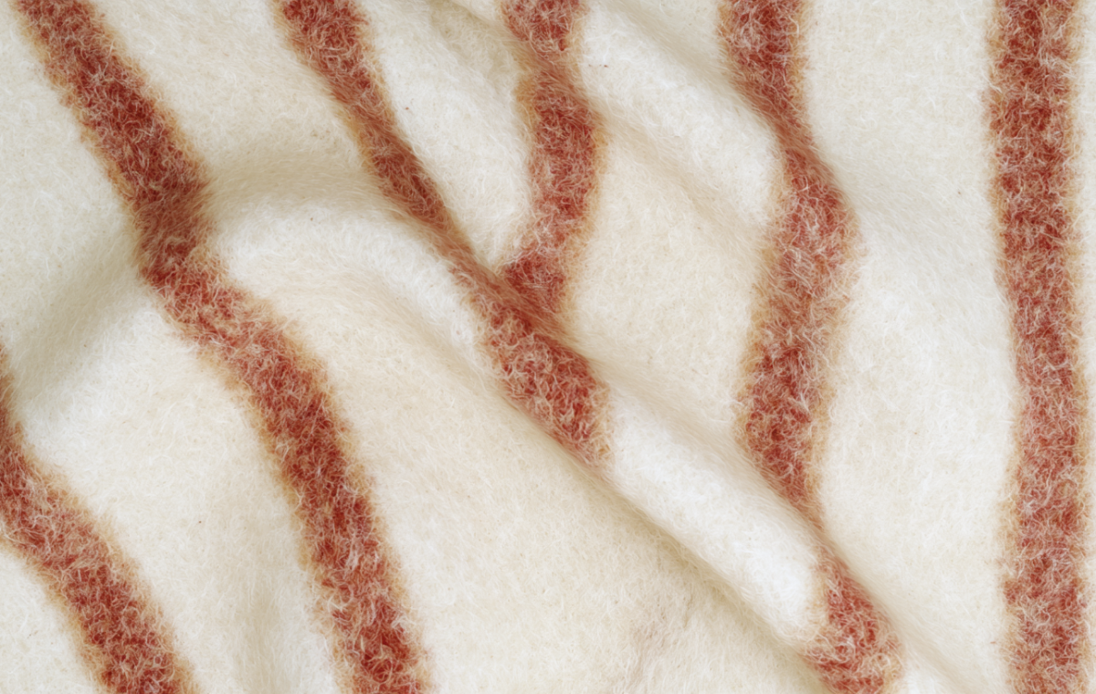 Close-up of a cozy cream and rust striped wool blanket with visible soft texture and folds in a living room setting.