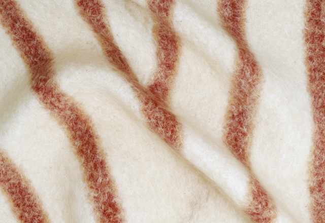 Close-up of a cozy cream and rust striped wool blanket with visible soft texture and folds in a living room setting.