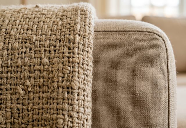 A close-up view of a heavy textured throw blanket draped over a neutral sofa arm.