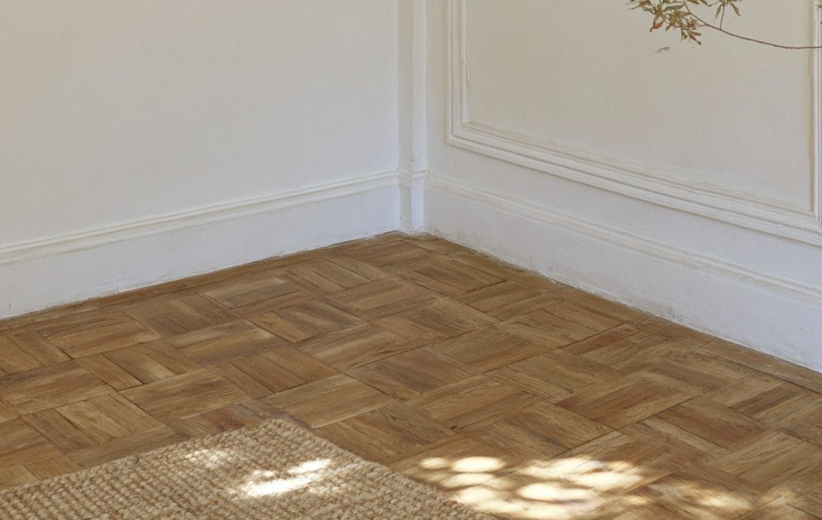 Close-up of geometric wooden parquet flooring in a room with white walls and a jute rug.