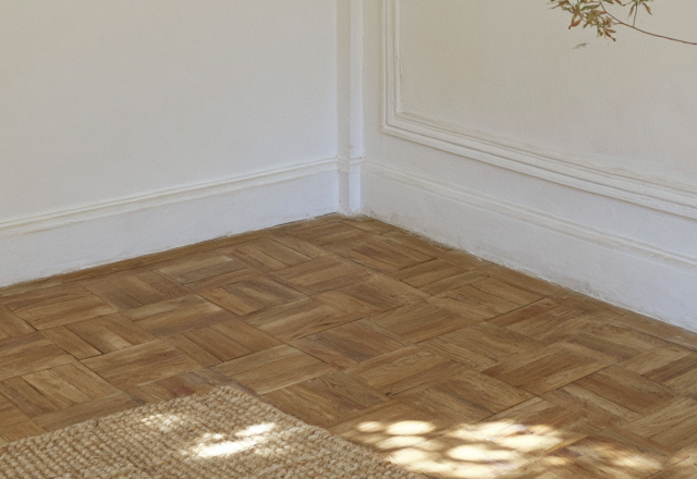 Close-up of geometric wooden parquet flooring in a room with white walls and a jute rug.