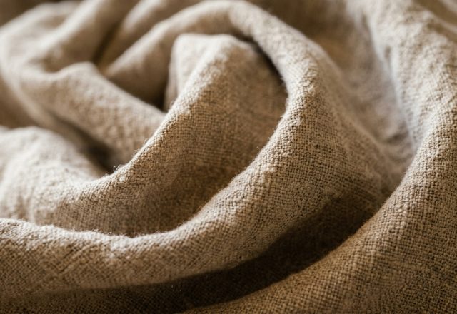Close-up shot of tumbled neutral linen fabric showing rich texture and organic folds.