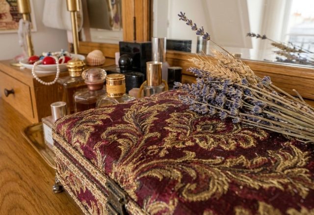 Close-up of a velvet vanity box and perfume bottles on a wooden dressing table with dried lavender.