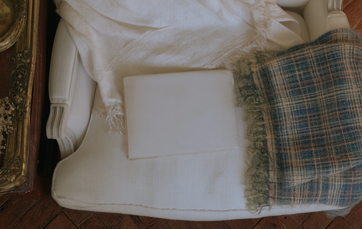 Vintage armchair styling featuring a white upholstered chair, plaid throw blanket, and antique brass frame.