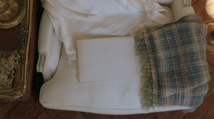 Vintage armchair styling featuring a white upholstered chair, plaid throw blanket, and antique brass frame.