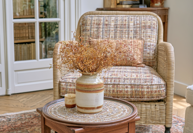 Vintage armchair styling with a patterned plaid chair, ceramic vase with dried stems, and a wooden coffee table in a bright sitting room.