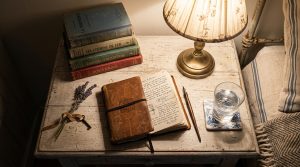 Vintage bedside table decor featuring antique books, a brass lamp, a leather journal, and dried lavender.