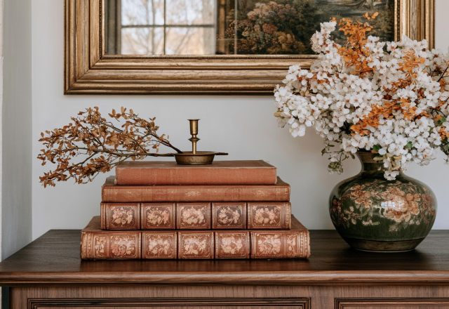 Vintage book decor styled on a wooden sideboard with a brass candle and floral vase